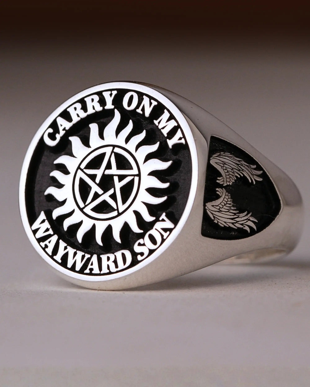 Sterling silver signet ring engraved with a sun and pentagram emblem and the words Carry On My Wayward Son