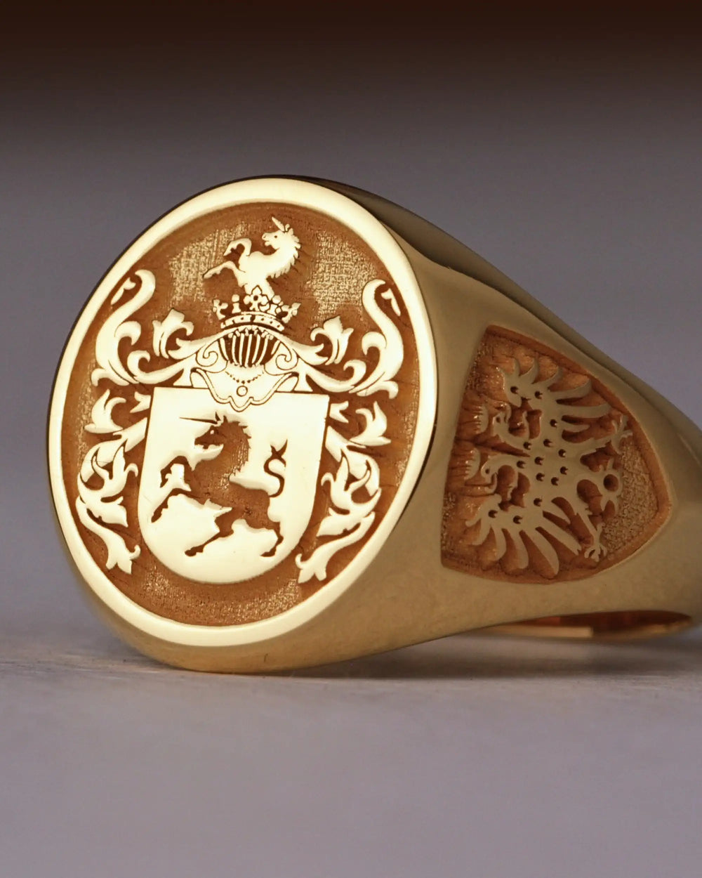 Gold-finish oval signet ring engraved with a family crest featuring a unicorn and a crowned helm, an eagle on the side